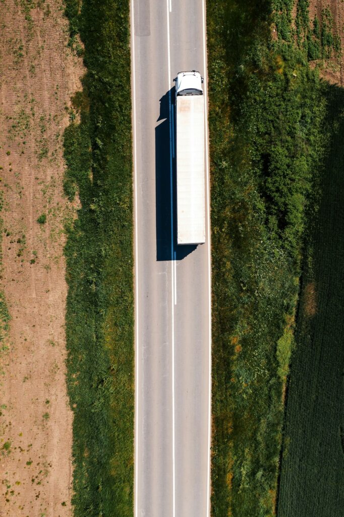 Aerial shot of semi-truck driving along the highway through countryside landscape, drone pov